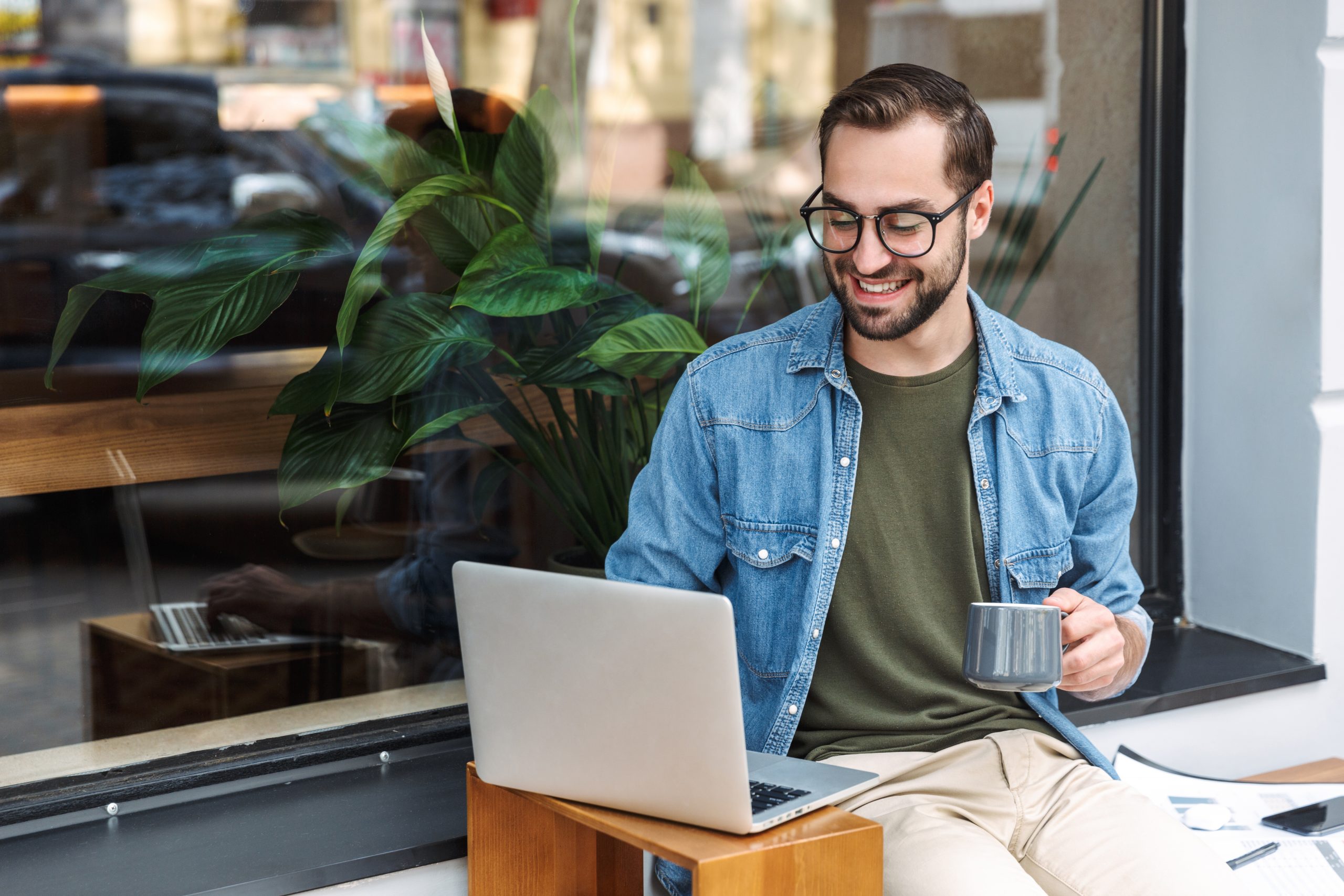 Photo of caucasian young man holding cup of coffee and typing on